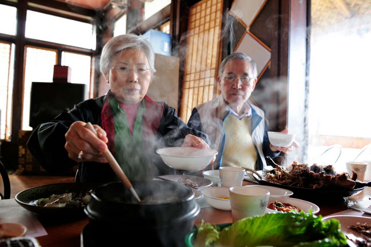 Asian Grandmother (70 years old) serving soup to her family with the Asian Grandfather (75 years old) sitting next to her on location at an Asian Restaurant